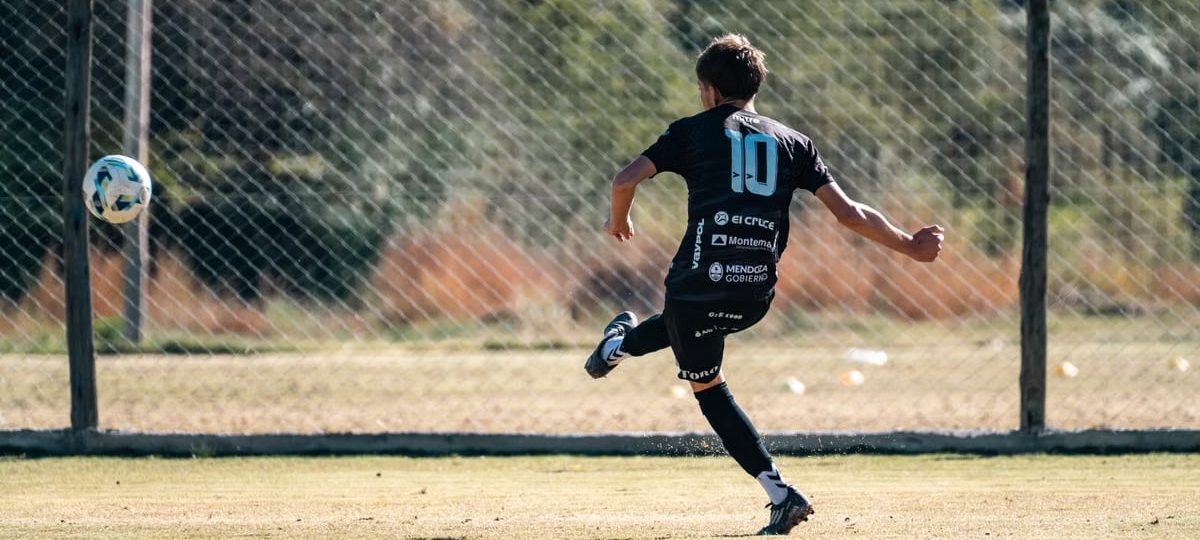 Youth soccer player in motion kicking a ball on a sunny outdoor field.