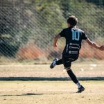 Youth soccer player in motion kicking a ball on a sunny outdoor field.