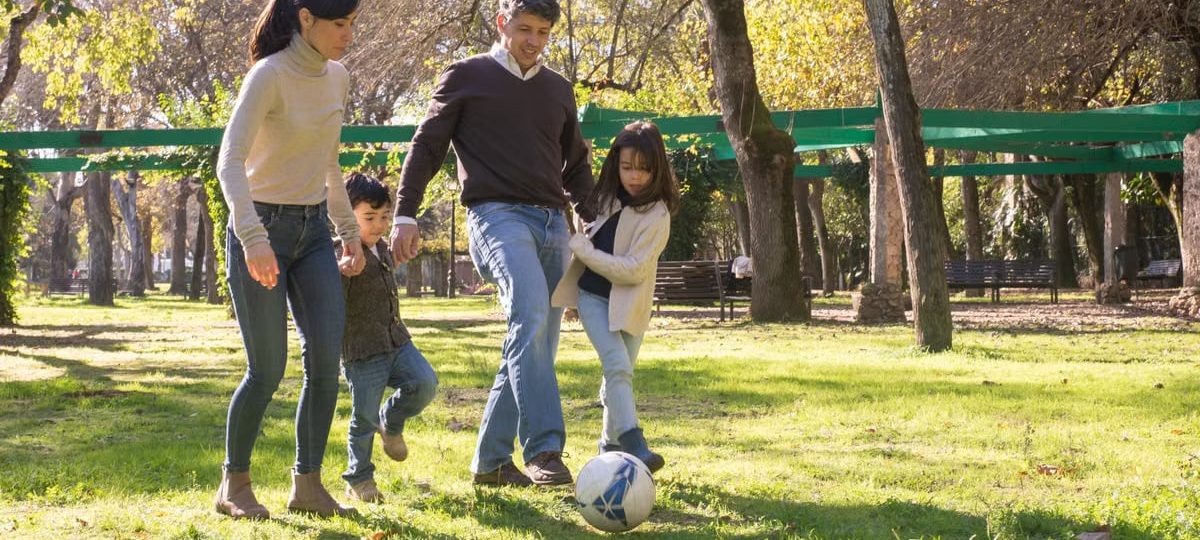 A family plays soccer together in a sunny park, enjoying quality time outdoors.